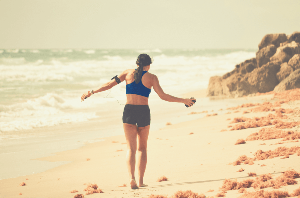 a woman walking down the beach holding heart rate monitor